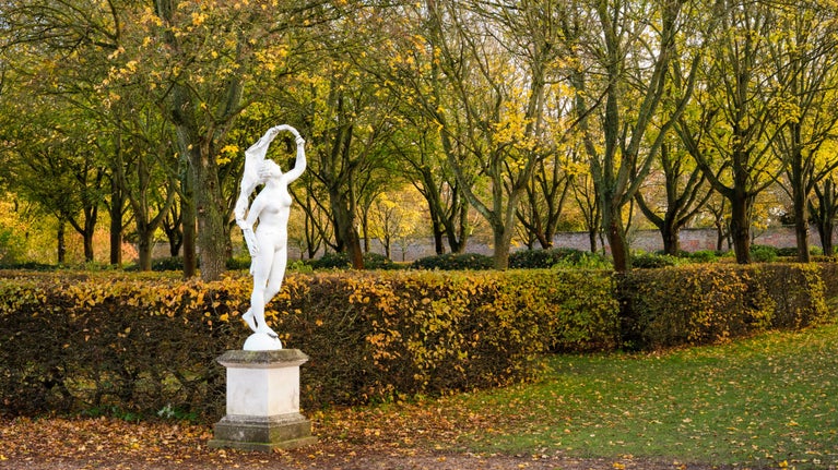 Statue of Fortuna, in the Wilderness at Ham House and Garden, London with yellow leaves on trees and hedges